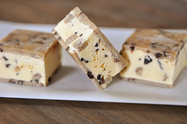A plate with three cookie dough ice cream sandwiches on it. The middle one is tipped to the side. 