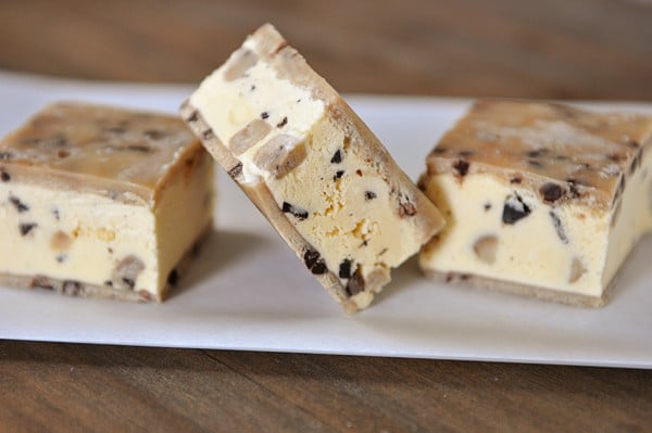 A plate with three cookie dough ice cream sandwiches on it. The middle one is tipped to the side.