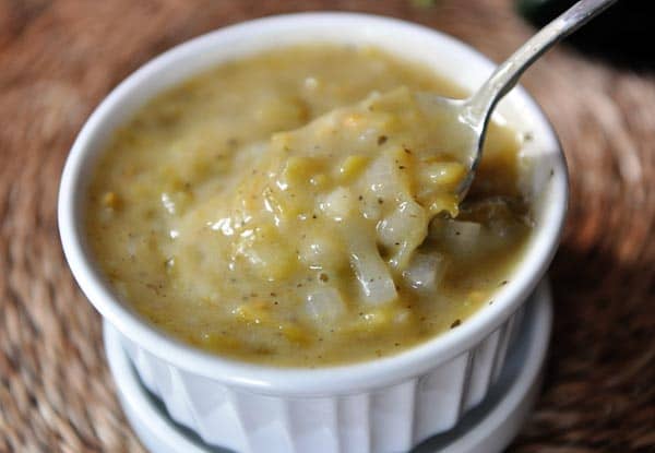 A spoon scooping green enchilada sauce out of a small white ramekin. 