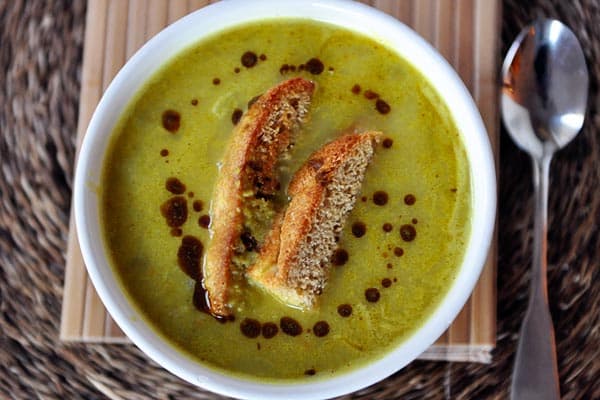 top view of a white bowl filled with green soup and pieces of bread dipped in the soup