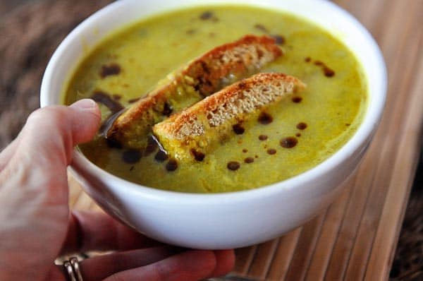 A hand holding a white bowl with green soup with two pieces of bread in the middle.