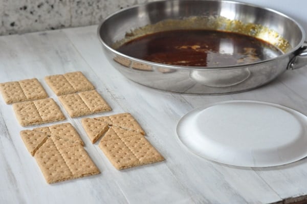 graham crackers, a white plate, and a pan of melted sugar on a table