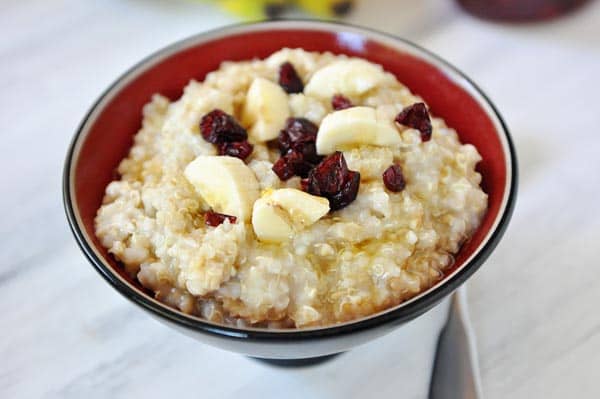 A bowl of cooked steel cut oats topped with banana slices and cranberries.