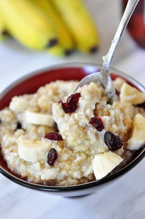 A bowl of cooked steel cut oats topped with bananas and dried cranberries.