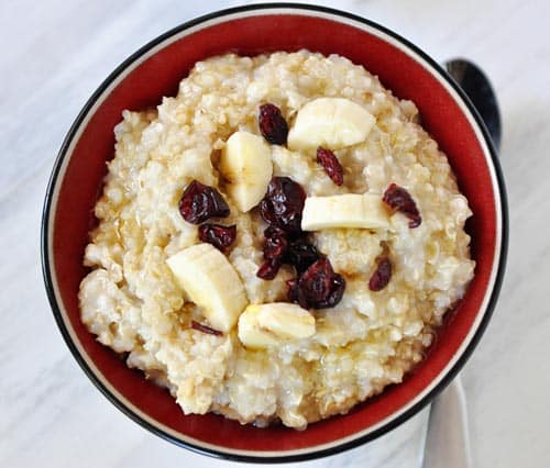 Top view of cooked steel cut oats with bananas and dried cranberries on top.