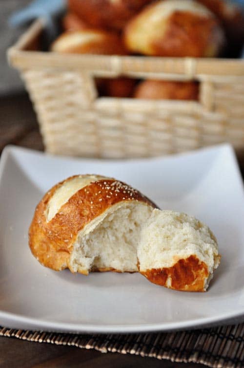 A golden brown pretzel roll with a chunk split off on a white plate.