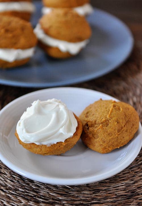 A pumpkin cream sandwich on a white plate with the top of the cookie sitting on the side.