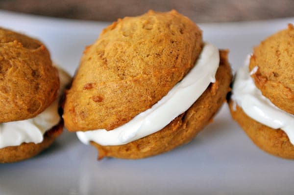 Three pumpkin cream-filled sandwiches lined up on a white platter.