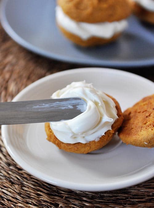 A pumpkin cookie getting frosted with a metal offset spatula.