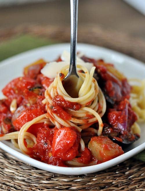 Plate of cooked spaghetti coated with a chunky red spaghetti sauce and a fork taking a bite out of the middle.