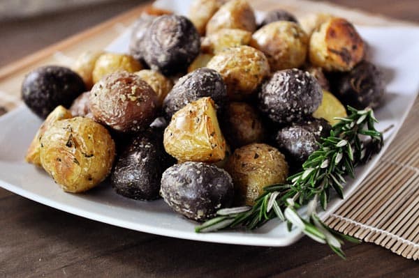 White platter with small cooked potatoes and a sprig of rosemary on the side.