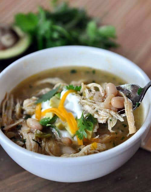 White bowl of white bean chicken chili with a spoon taking a bite out.