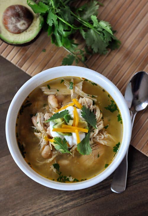 Top view of a white bowl full of white bean chicken chili topped with parsley leaves and a dollop of sour cream.