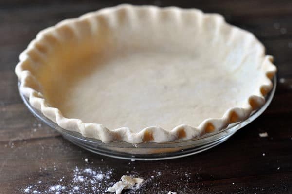 A raw crimped pie crust in a glass pie pan. 