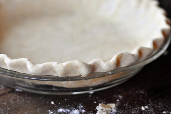 Side view of an uncooked crimped pie crust in a glass pie dish.