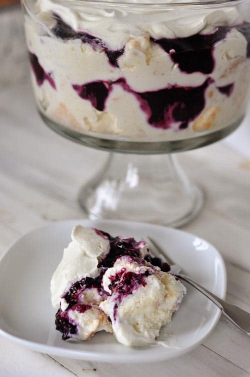 A plate with a white cake and blueberry dessert, with a trifle dish full of the dessert in the background.