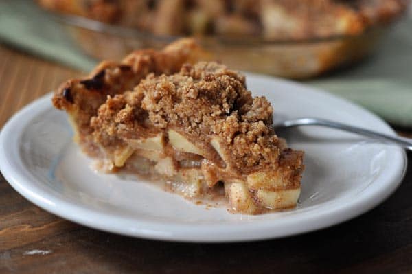 A slice of apple crumb pie on a white plate.