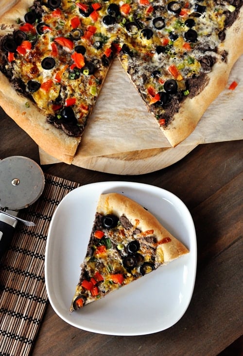 Top view of a veggie-topped black bean pizza with a slice taken out on a white plate.