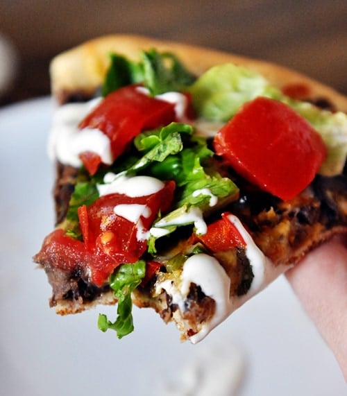 A slice of black bean pizza with a bite taken out and lettuce and tomatoes on top.