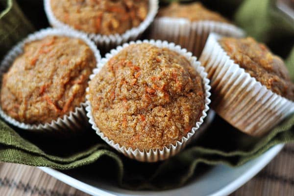 Five carrot cake muffins in white liners sitting on top of a green napkin in a bowl. 