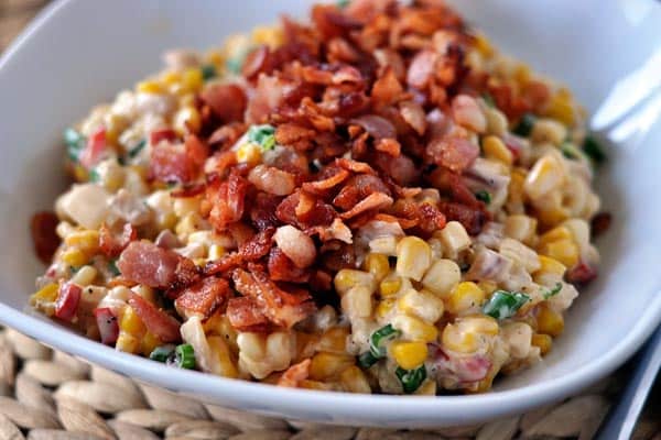 A bowl of creamy confetti corn with crispy, chopped bacon sprinkled over the top. 