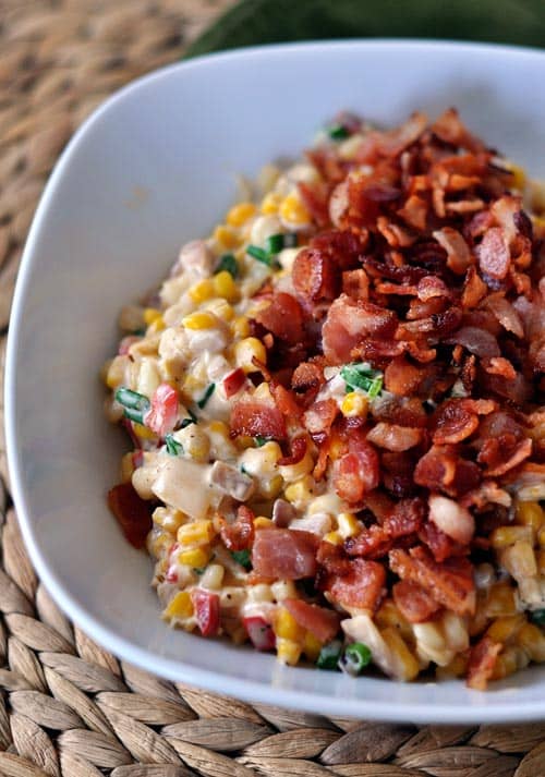 A bowl of creamy confetti corn with crispy, chopped bacon sprinkled over the top. 