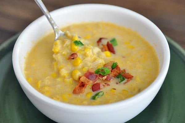 A white bowl of corn chowder with little bits of bacon and a few sliced green onions on top.