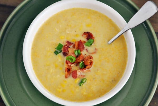 Top view of white bowl full of corn chowder topped with sliced green onions and chopped bacon.