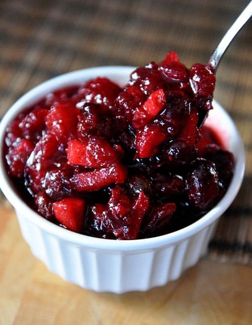 white ramekin full of fresh cranberry chutney with a spoon taking a bite out