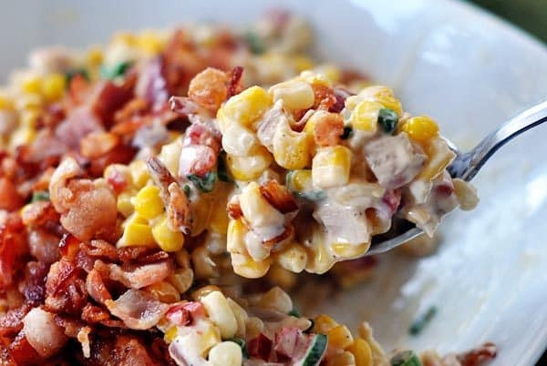 A spoon taking out a bite of creamy corn topped with bacon. 