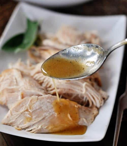 White platter of turkey breast with a spoon drizzling gravy over the top.