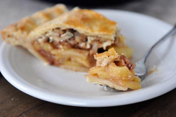 a slice of apple pie on a white plate with a fork taking a bite out