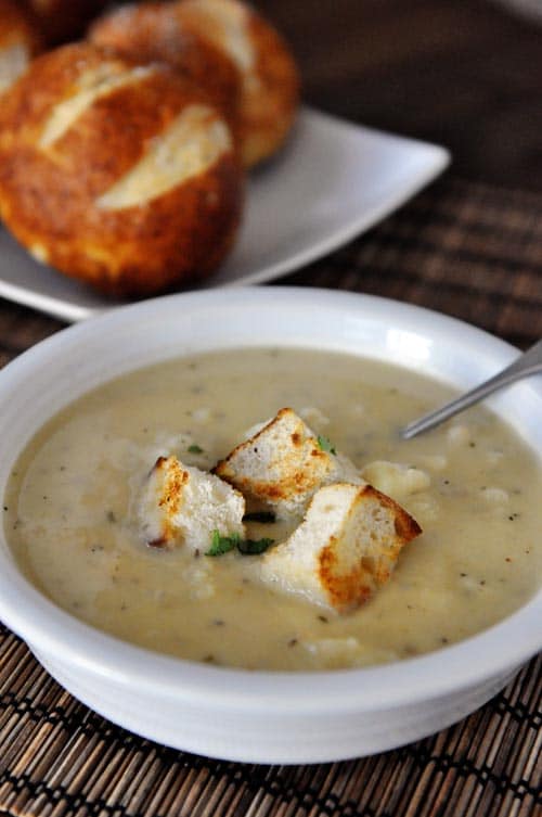 White bowl full of cauliflower soup with three big croutons on top.