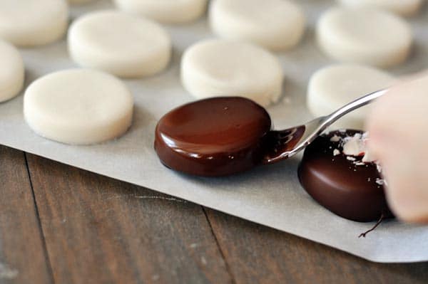 A homemade circular mint patty that was just dipped in chocolate, surrounded by mint patties ready to be dipped.