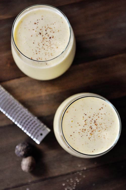 Top view of two glass cups full of eggnog sprinkled with freshly grated nutmeg.