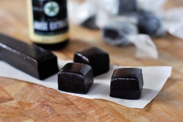 Pieces of licorice caramels cut off a log of caramel on a piece of parchment.