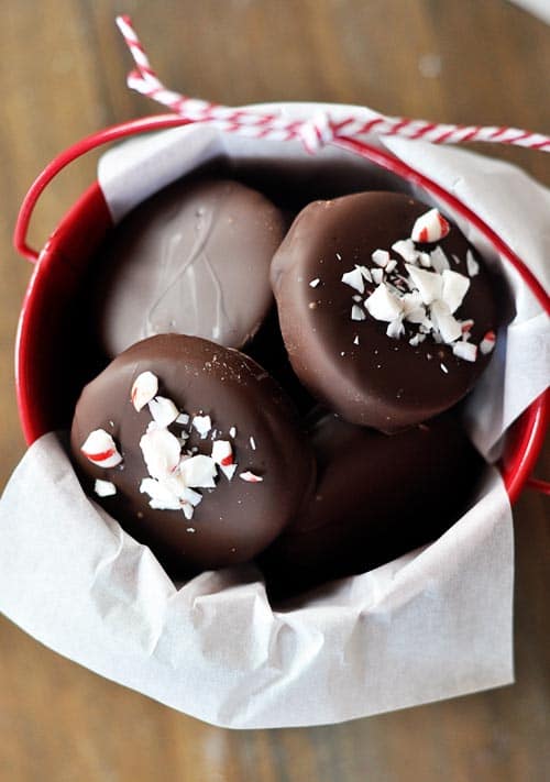 Homemade chocolate-dipped peppermint patties, with crushed candy canes on top of each patty, all in a small red bucket.