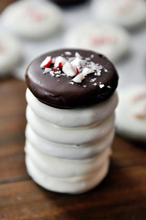 A stack of white chocolate dipped cookies with a chocolate dipped cookie on top covered in crushed candy canes.