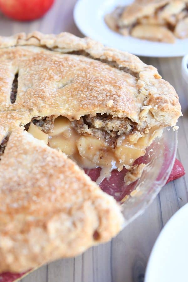 Toffee crumble caramel apple pie in glass pie plate with slice removed.