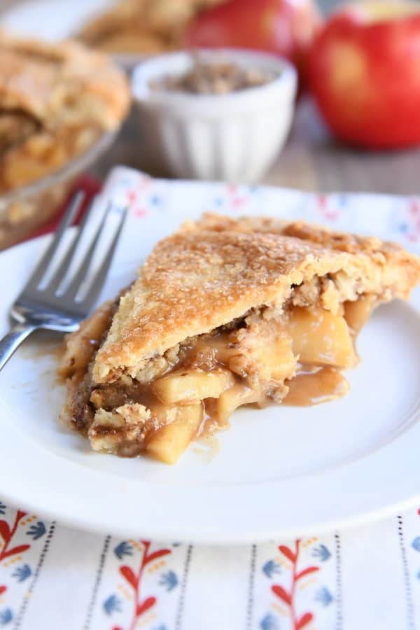 Slice of toffee crumble caramel apple pie on white plate.