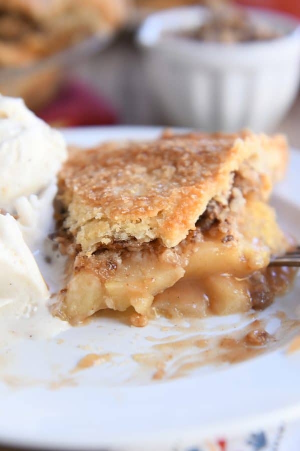 Half a slice of apple pie on white plate with vanilla ice cream.