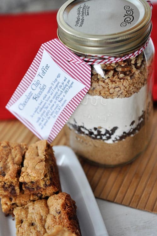 a mason jar full of layered dry ingredients to make chocolate chip toffee blondies with cooked blondies on the side