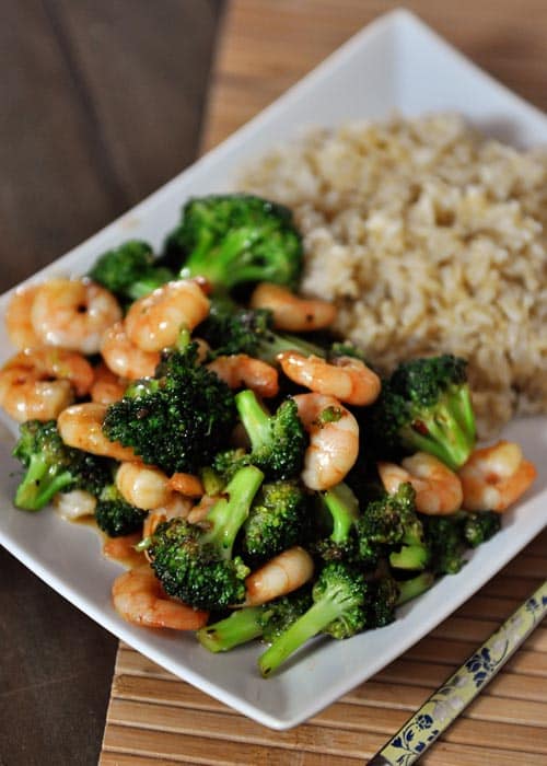 White platter full of cooked broccoli and shrimp next to a serving of cooked brown rice.
