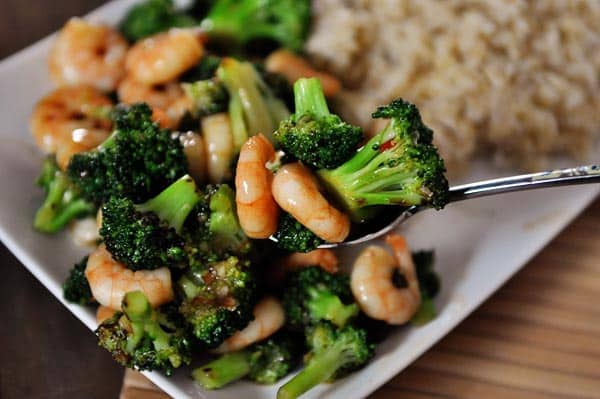 Cooked broccoli and shrimp next to cooked brown rice on a white platter.