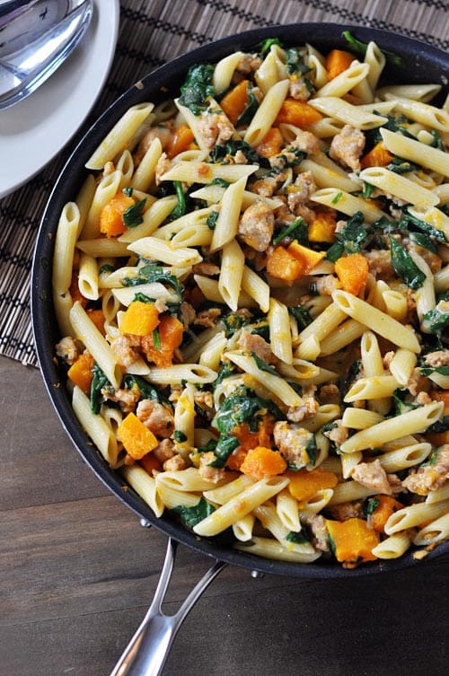 A skillet full of tube pasta, butternut squash, spinach, and sausage.