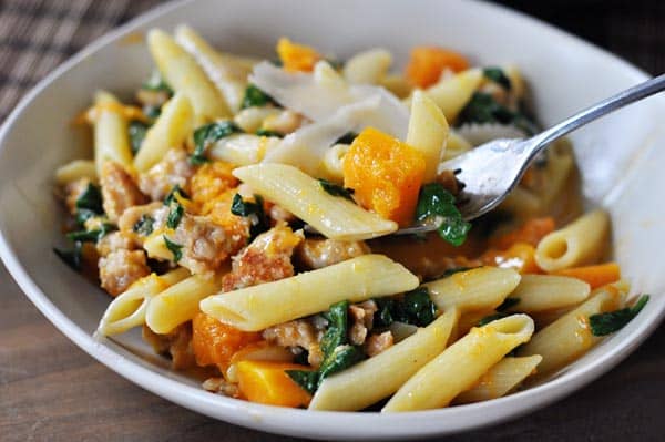 White bowl with tube pasta, squash, sausage, and spinach.