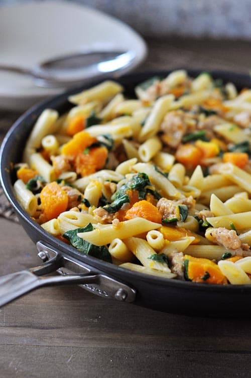 Skillet full of pasta, spinach, cubes of butternut squash, and cooked sausage.