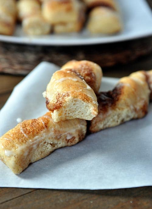 Piece of parchment with two cinnamon and sugar breadsticks with one of them with a bite taken out.