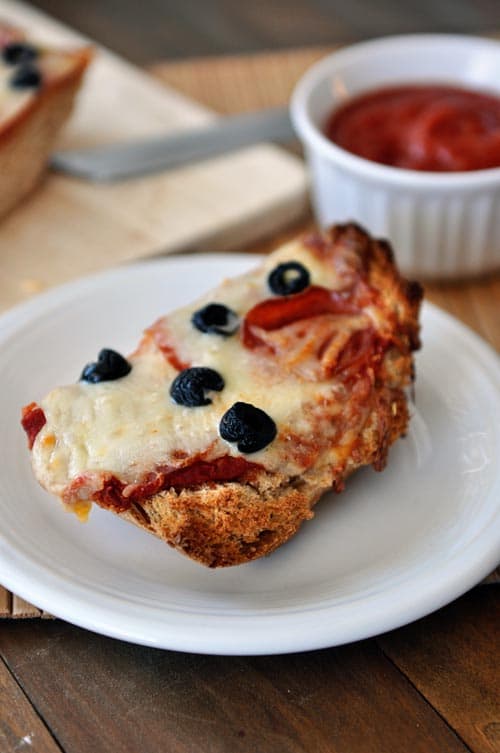 A slice of cooked pepperoni olive french bread pizza on a white plate.