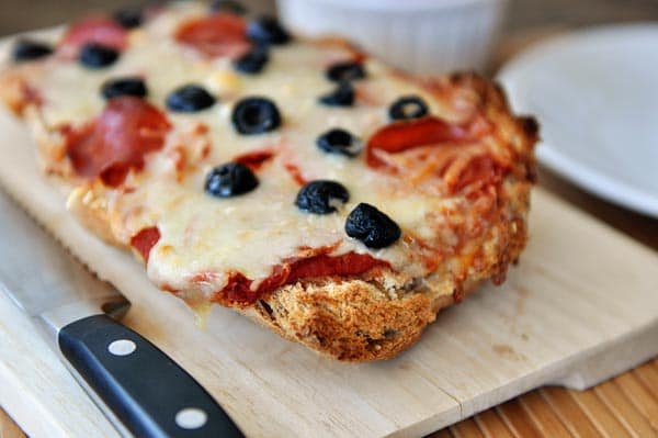 A pepperoni and olive-topped french bread pizza on a cutting board.